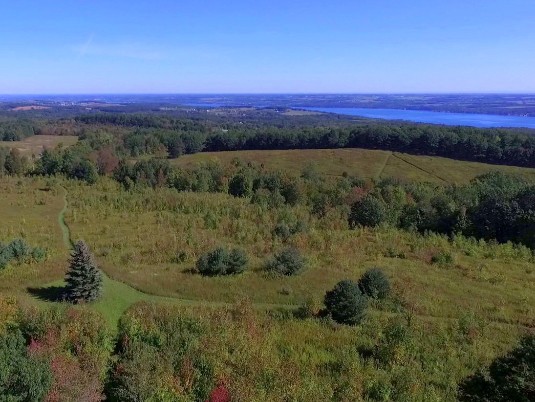 A drone view of fields and trails with a lake in the distance