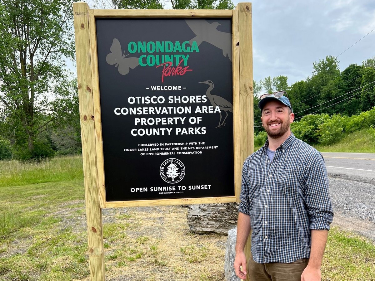 A person standing next to a new county park sign 
