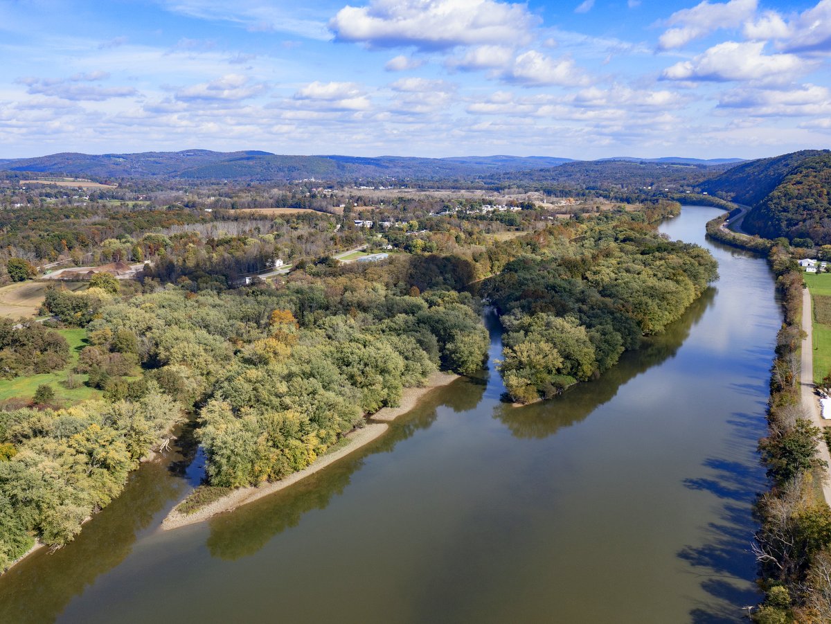 An aerial view of a river with two forested islands and hills in the distance