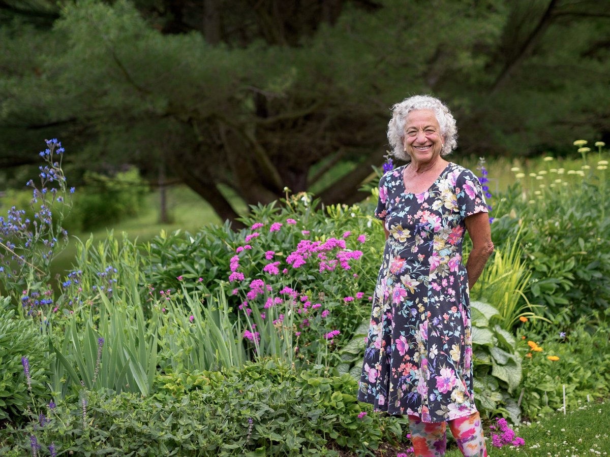 A woman wearing a flowery dress standing in front of her flower garden