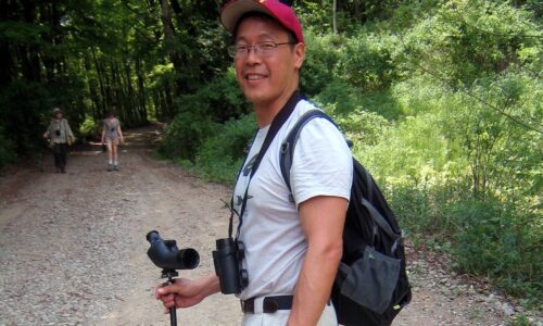 A person standing on a trail with a spotting scope for birding