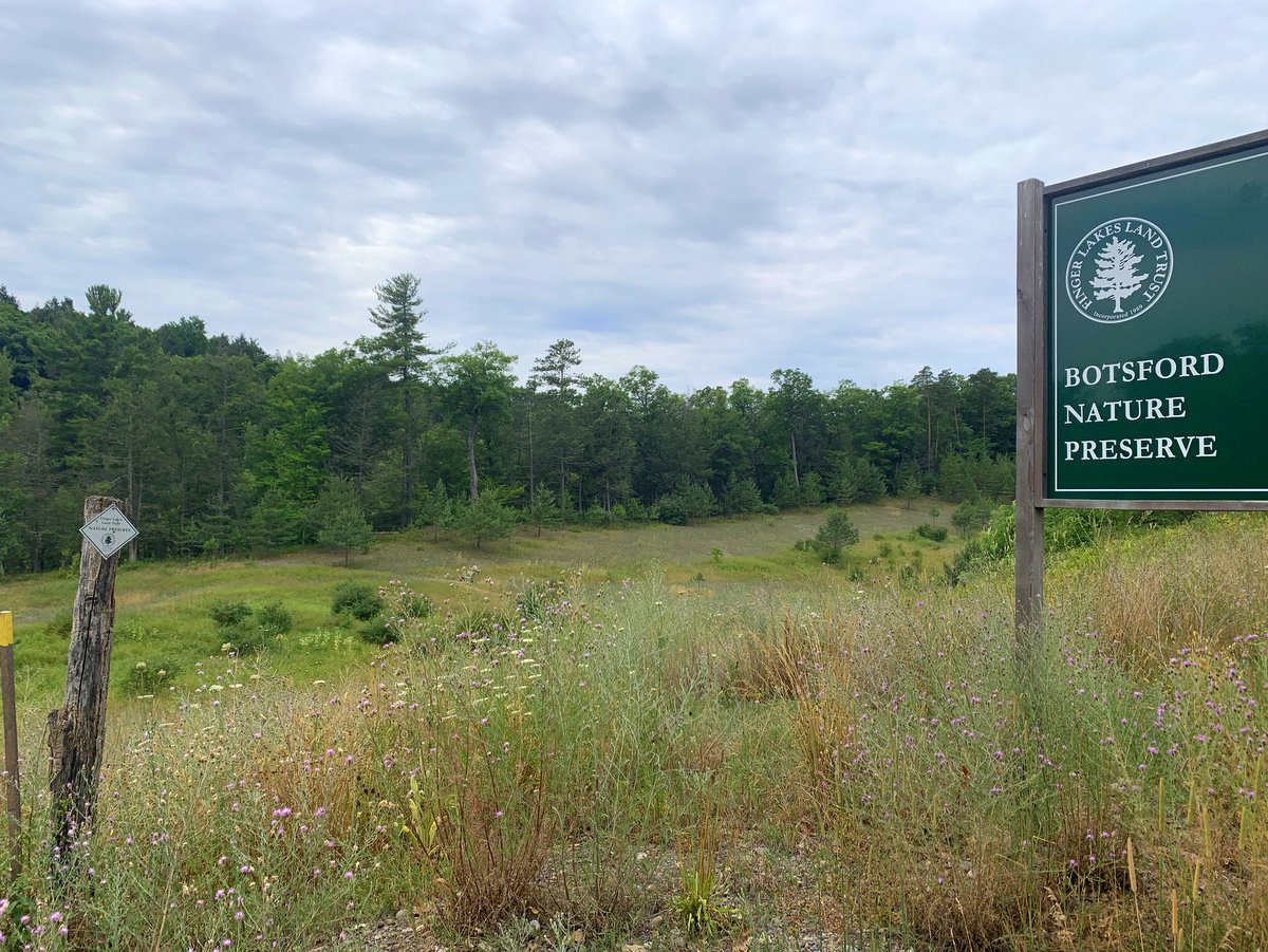 A nature preserve sign and trailhead leading to a meadow
