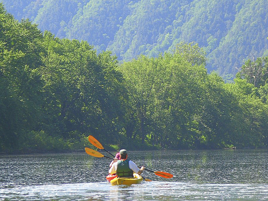 Two people kayaking on a river with green hills in the foreground 